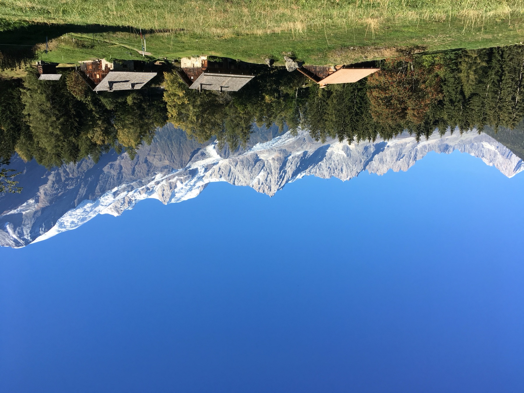 Mountain chalets in a green meadow below snowy peaks